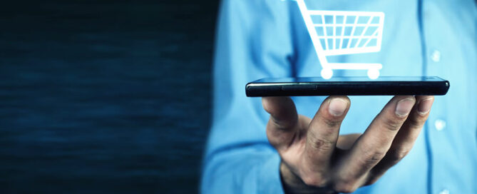 Mann hält Handy mit virtuellem Einkaufswagen - E-Commerce
