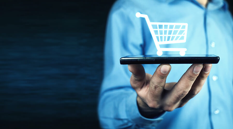 Mann hält Handy mit virtuellem Einkaufswagen - E-Commerce